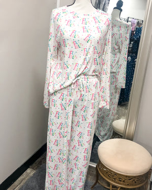 A white pajama set with "FA LA LA" and small sparkle shapes printed in pastel pinks, greens, and blues. The top is a medium-width necked sweatshirt and the bottoms are draw stringed sweatpants.