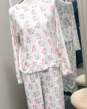 A white pajama set with "FA LA LA" and small sparkle shapes printed in pastel pinks, greens, and blues. The top is a medium-width necked sweatshirt and the bottoms are draw stringed sweatpants.